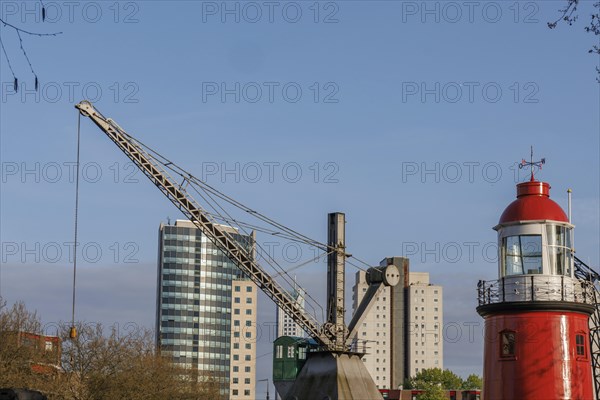 A red lighthouse and a crane in front of modern buildings and a calm sky, small harbour in a big city with a lighthouse and modern houses, Rotterdam, Netherlands