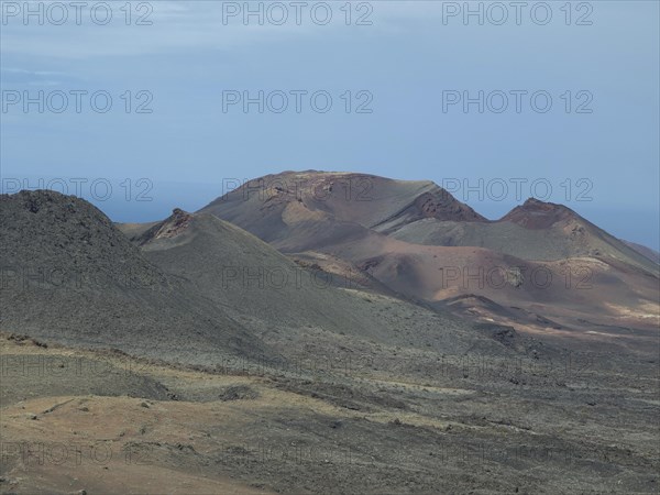 Rocky volcanic landscape with hills and a view of the sea in the background, barren landscape with roads, craters and small bushes, Lanzarote, spain