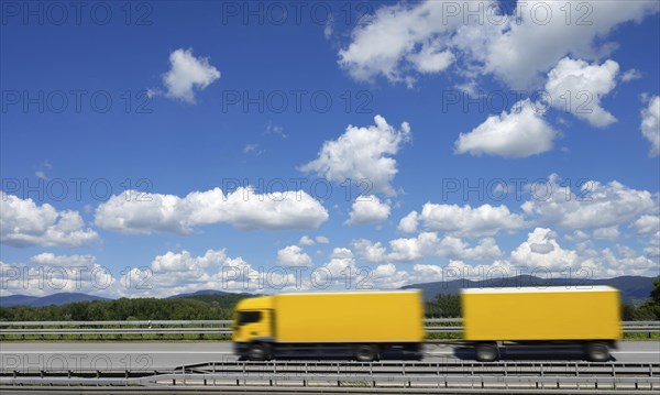 A yellow lorry drives on the A3 motorway under a blue sky with white clouds, motion blur, Bavarian Forest in the background, Deggendorf, Bavaria, Germany, Europe
