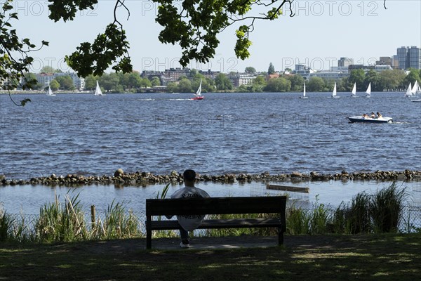 Symbolic picture weather, leisure activity, summery spring, silhouette of a man on a park bench, behind him sailboats and pedal boats against a blue sky on the Alster in Hamburg, Germany, Europe