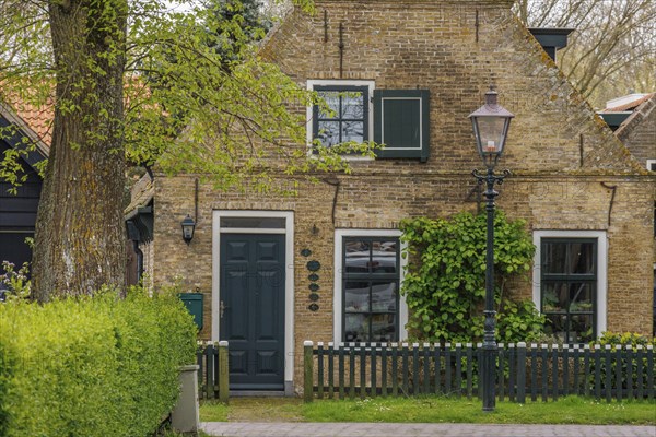 Narrow brick house with garden fence and shutters, flanked by trees, old houses with green gardens in a small village, nes, ameland, the netherlands