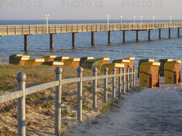 Several beach chairs on a sandy path leading to a jetty into the sea at sunset, beach chairs in the morning light with blue sky by the sea, pier in the sea, Binz, Germany, Europe
