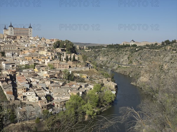 Historic cityscape on the river, architecturally solidly built, surrounded by hills with characteristic church towers and under a clear sky, historic city with old houses and large churches on a small river against a blue sky, toledo, spain