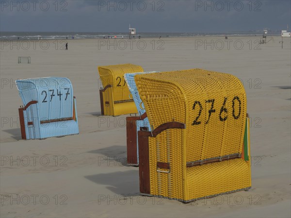 Yellow and blue beach chairs in a sandy landscape on a cloudy day, colourful beach chairs on the beach and in the dunes on a cloudy day, red wooden boat and yellow beach chair, Juist, Germany, Europe