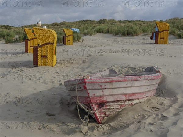 Abandoned boat in the sand, surrounded by beach chairs and dunes, cloudy sky in the background, colourful beach chairs on the beach and in the dunes with overcast sky, red wooden boat and yellow beach chair, Juist, Germany, Europe