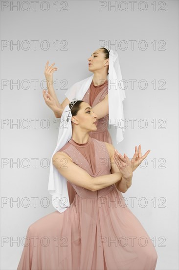 Two female dancers perform hand movements on grey background