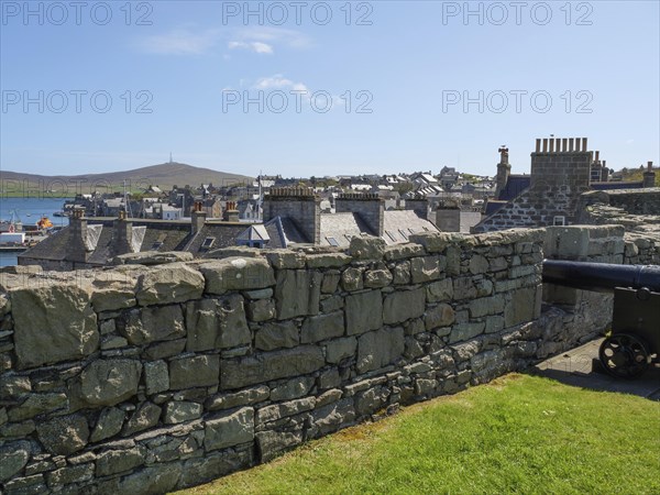 An old cannon behind a wall with a view of the town and hills, old cannons on a stone wall by the sea against a blue sky, lerwick, Scotland, United Kingdom, Europe