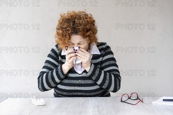 A woman with a red head and black and gray striped sweater is blowing her nose