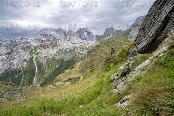 Mountaineer on a narrow hiking trail on a steep meadow slope, descent from the Raudenspitze, view into the Val Fleons valley with rocky mountain peaks, Carnic Main Ridge, Carnic Alps, Carinthia, Austria, Europe