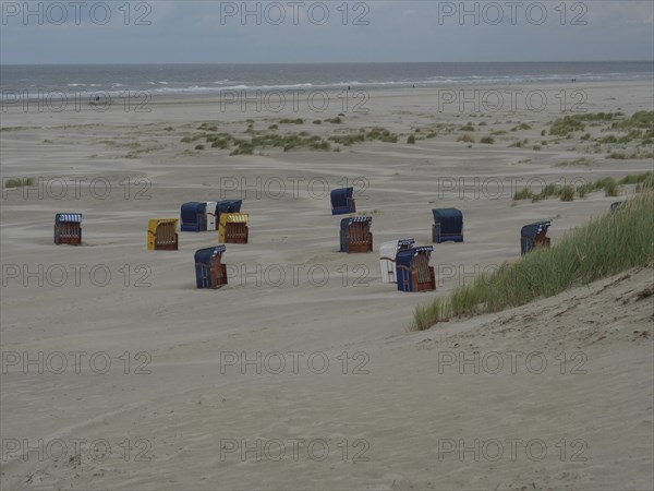 Abandoned beach chairs are scattered on the sandy beach in front of a cloudy coastline, colourful beach chairs on the beach and in the dunes under cloudy sky, red wooden boat and yellow beach chair, Juist, Germany, Europe