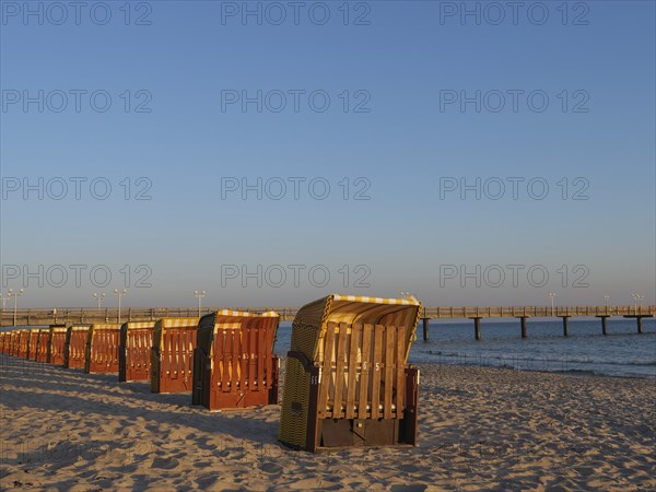 Beach chairs along the beach at sunset with a pier extending into the sea, beach chairs in the morning light with blue sky by the sea, pier in the sea, Binz, Germany, Europe