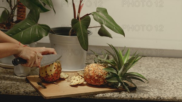 A persons' hands peeling a pineapple fruit using a knife to make a healthy vegan summer snack