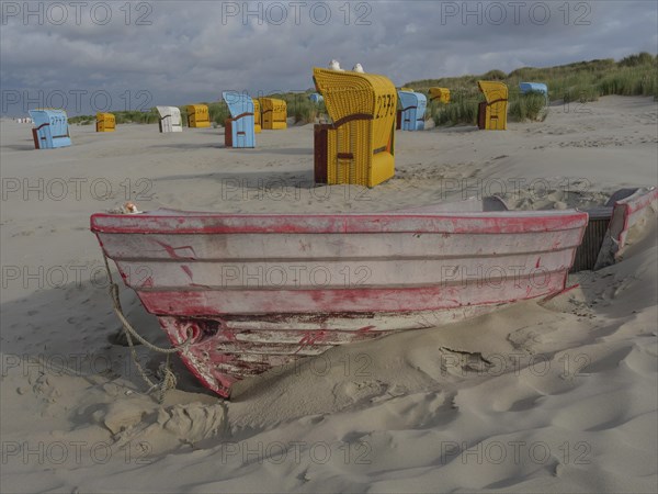 Red boat in the sand with scattered beach chairs and dunes, peaceful atmosphere, colourful beach chairs on the beach and in the dunes with overcast sky, red wooden boat and yellow beach chair, Juist, Germany, Europe