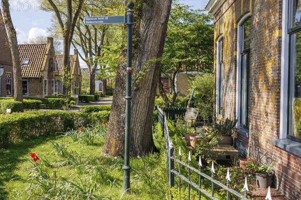 An idyllic village with manicured gardens, blooming flowers and a street sign, historic houses and a church with small streets and lanterns, Nes, Ameland, Netherlands