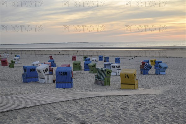 Atmospheric evening sun on a quiet beach with colourful beach chairs and a wooden walkway in the sand, many colourful beach chairs on a balmy summer evening by the sea, langeoog, germany