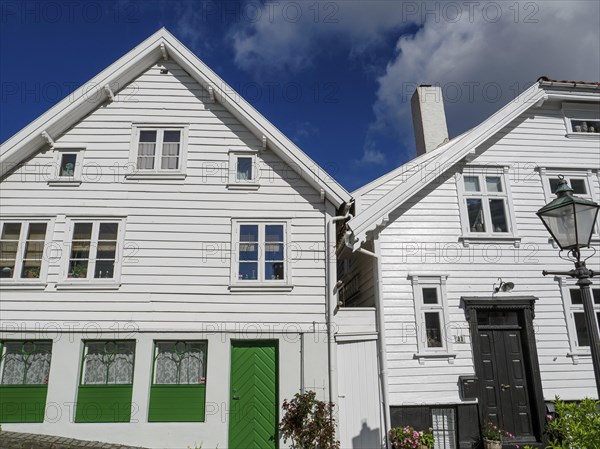 Historic white wooden houses with green doors and windows under a blue sky, illuminated during the day, white wooden houses with green trees and flowers against a blue sky, Stavanger, Norway, Europe