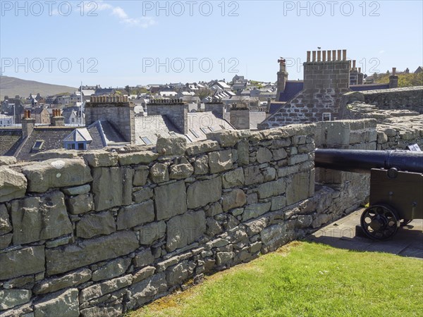 A cannon stands behind a stone wall overlooking the town, old cannons on a stone wall by the sea against a blue sky, lerwick, Scotland, United Kingdom, Europe