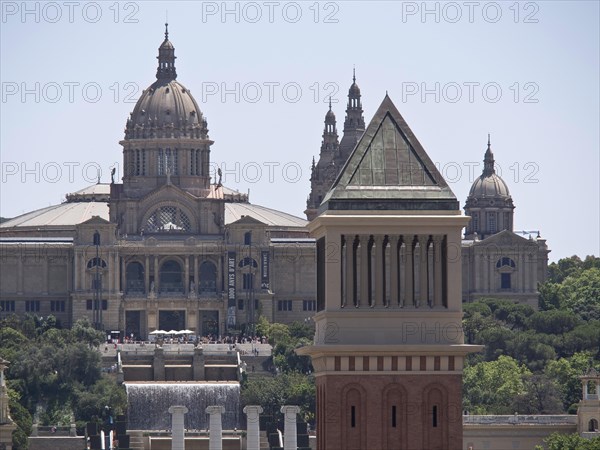 Close-up of a historic building with a magnificent dome and detailed tower against the background of a clear sky, two red towers against the panorama of a large city, Barcelona, Spain, Europe