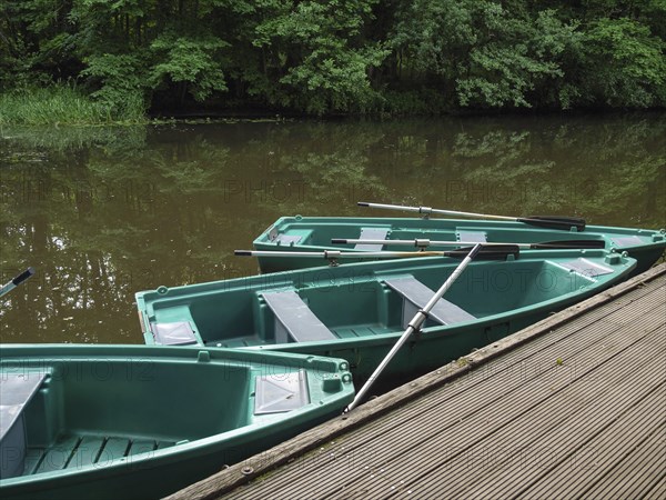Green boats on a wooden jetty on a quiet river with trees in the background, green rowing boats on a jetty, river in the forest with many trees, ahaus, germany