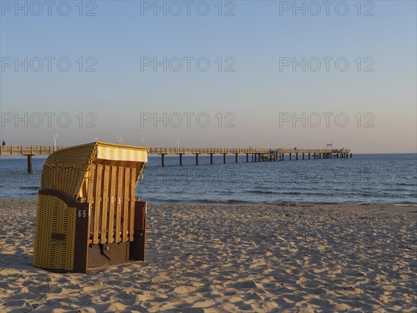 Single beach chair on a sandy beach in the evening sunlight, with a pier in the background, beach chairs in the morning light with blue sky at the sea, pier in the sea, Binz, Germany, Europe