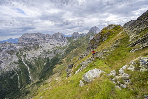 Mountaineer on a narrow hiking trail on a steep meadow slope, descent from the Raudenspitze, view into the Val Fleons valley with rocky mountain peaks, Carnic Main Ridge, Carnic Alps, Carinthia, Austria, Europe
