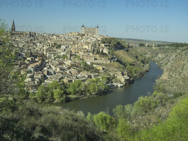 Historic city on the river with impressive architecture and striking church towers, situated on a hill under a blue sky, historic city with old houses and large churches on a small river in front of a blue sky, toledo, spain