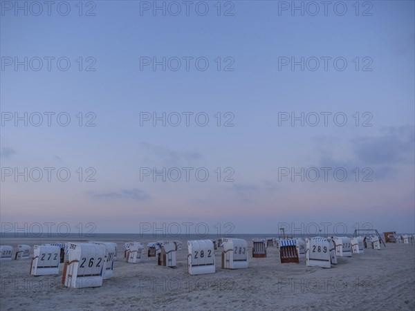 A peaceful scene on the beach with white and striped beach chairs during dusk, setting sun on a beach with beach chairs and clouds in the sky, spiekeroog, germany