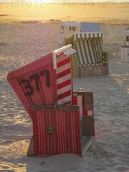 Red and white beach chair on a sandy beach at sunset, sunset on a quiet beach with many colourful beach chairs, warm evening light by the sea, Langeoog, GERMANY