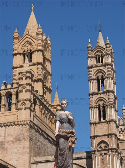 Historic cathedral with detailed towers and a central statue, under a bright blue sky, two red towers in front of a panorama of a large city, Barcelona, Spain, Europe