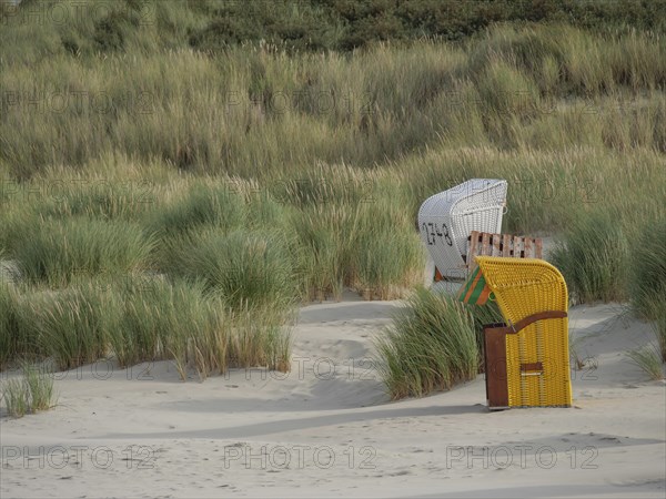 A quiet beach landscape with beach chairs and grasses in front of the dunes under a cloudy sky, colourful beach chairs on the beach and in the dunes under a cloudy sky, red wooden boat and yellow beach chair, Juist, Germany, Europe