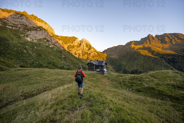 Mountaineers on the way to the Alpine Club hut, Hochweisssteinhaus mountain hut, mountain landscape with green mountain meadows and rocky peaks at sunrise, alpenglow, Carnic High Trail, Carnic Main Ridge, Carnic Alps, Carinthia, Austria, Europe