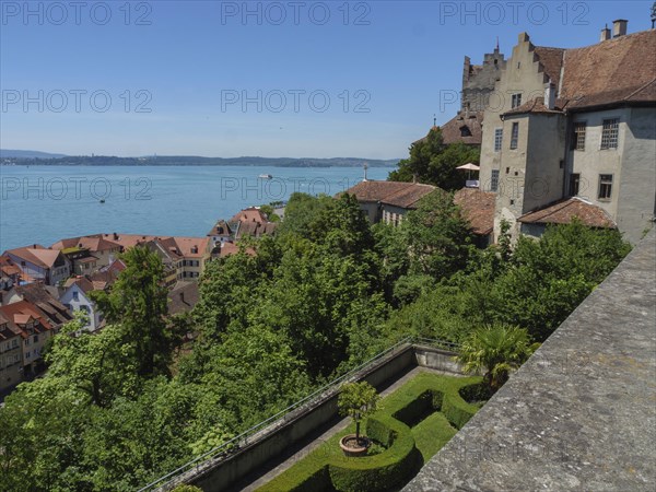 View of a castle with a wide view over roofs and trees to a lake, old buildings with many trees on a large lake, meersburg, germany