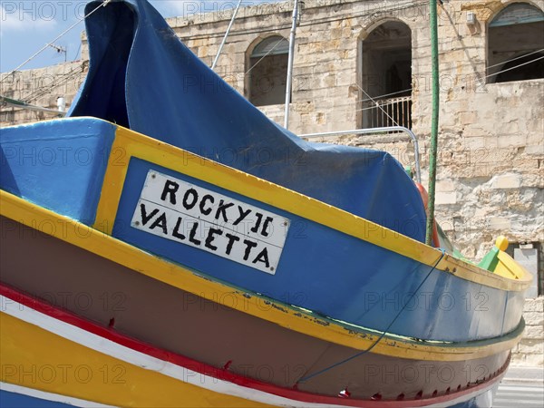 Side view of a colourful boat with cover and the inscription ROCKY II VALLETTA, many colourful fishing boats in a harbour in the Mediterranean Sea, Marsaxlokk, malta