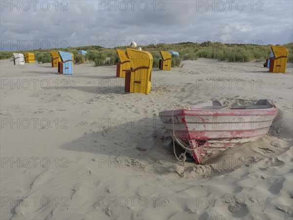 Empty boat on the beach with surrounding beach chairs and dunes, under a cloudy sky, colourful beach chairs on the beach and in the dunes under an overcast sky, red wooden boat and yellow beach chair, Juist, Germany, Europe
