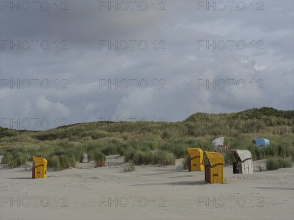 A wide dune landscape with scattered beach chairs under a cloudy sky, colourful beach chairs on the beach and in the dunes under an overcast sky, red wooden boat and yellow beach chair, Juist, Germany, Europe