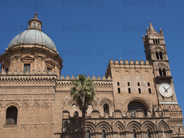 Side view of a historic cathedral with a striking dome and a clock on the tower, against a blue sky, two red towers in front of a panorama of a large city, Barcelona, Spain, Europe