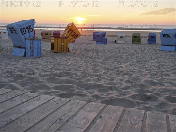 Various beach chairs on a sandy beach during sunset, sea in the background and a wooden walkway in the foreground, sunset on a quiet beach with many colourful beach chairs, warm evening light by the sea, Langeoog, GERMANY
