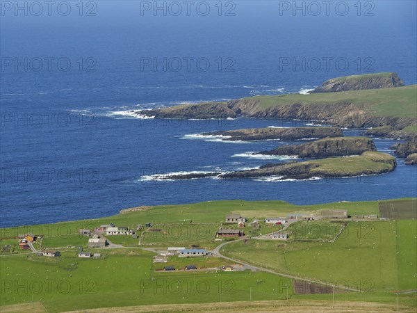 Coastal view of a small village with fields and islands in the background, calm sea with rocks and fields with historic houses, Lerwick, Shetlands, Scotland, United Kingdom, Europe