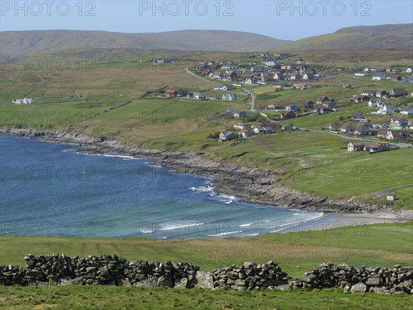 Coastal landscape with a small village on green hills overlooking the blue sea, calm sea with rocks and fields with historic houses, Lerwick, Shetlands, Scotland, United Kingdom, Europe