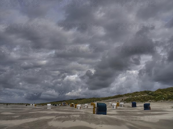 Various beach chairs stand in front of a cloudy sky on a deserted beach, colourful beach chairs on the beach and in the dunes under an overcast sky by the sea, Juist, Germany, Europe