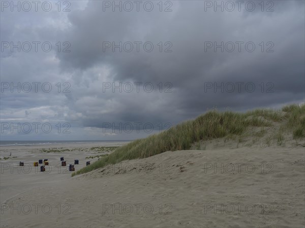 Large dunes and a cloudy sky frame the deserted beach chairs on the beach, colourful beach chairs on the beach and in the dunes under an overcast sky, red wooden boat and yellow beach chair, Juist, Germany, Europe
