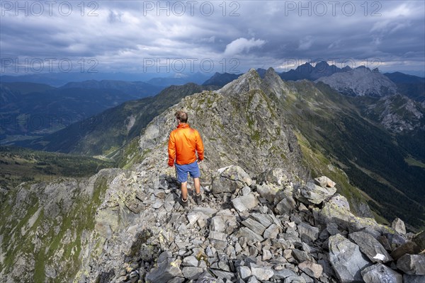 Mountaineer on the rocky pointed summit of the Raudenspitze or Monte Fleons, view of narrow mountain ridge, mountain panorama on the Carnic main ridge, Carnic Alps, Carinthia, Austria, Europe