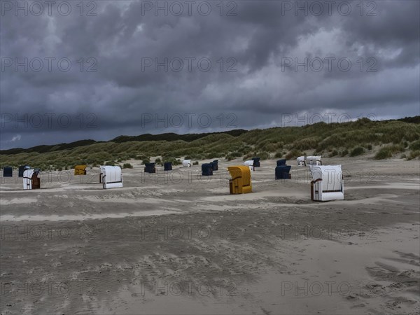 Beach chairs standing on a grey beach under a threatening cloudy sky, dunes in the background, colourful beach chairs on the beach and in the dunes under an overcast sky by the sea, Juist, Germany, Europe