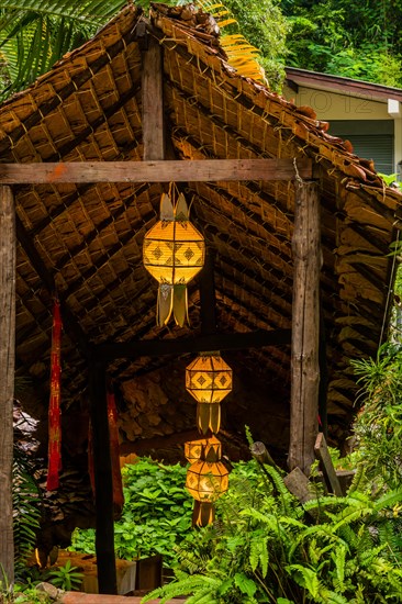Beautiful oriental lanterns hanging under covered walkway surrounded by lush green foliage in Thailand
