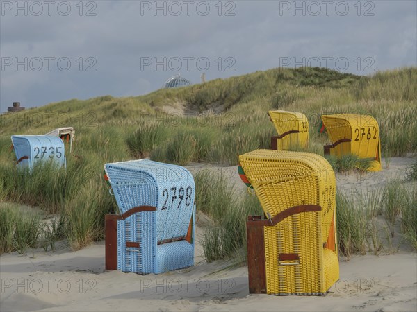 Different coloured beach chairs on the sandy beach, surrounded by dunes and under a cloudy sky, colourful beach chairs on the beach and in the dunes under a cloudy sky, red wooden boat and yellow beach chair, Juist, Germany, Europe