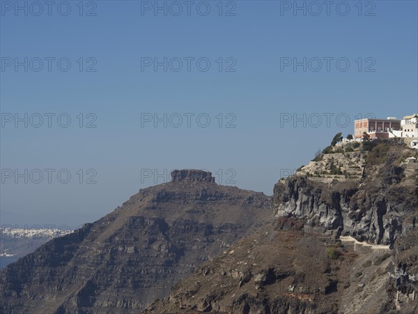 A prominent peak with houses standing high on the steep cliffs of Santorini, under a clear sky, rocky island in the sea with white houses against a blue sky, Santorini, Greece, Europe