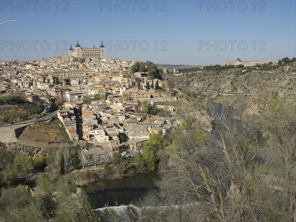 Panoramic view of a historic city on the river with characteristic buildings and church towers, surrounded by hills and nature under a clear sky, historic city with old houses and large churches on a small river in front of a blue sky, toledo, spain