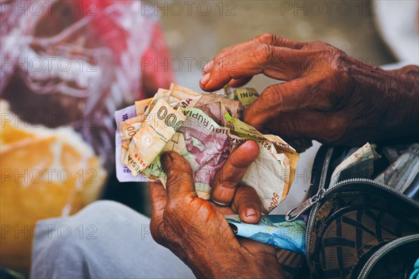Older hands counting weathered paper Indonesian currency called Indonesian Rupiah, suggesting a transaction, economy and inflation