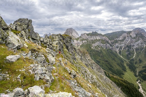 Mountaineer on a narrow rocky mountain path on a ridge, descent from the Raudenspitze, view into the Val Fleons valley with rocky mountain peaks, Carnic Main Ridge, Carnic Alps, Carinthia, Austria, Europe