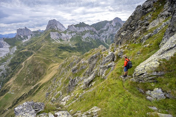Mountaineer on a narrow hiking trail on a steep meadow slope, descent from the Raudenspitze, view into the Val Fleons valley with rocky mountain peaks, Carnic Main Ridge, Carnic Alps, Carinthia, Austria, Europe